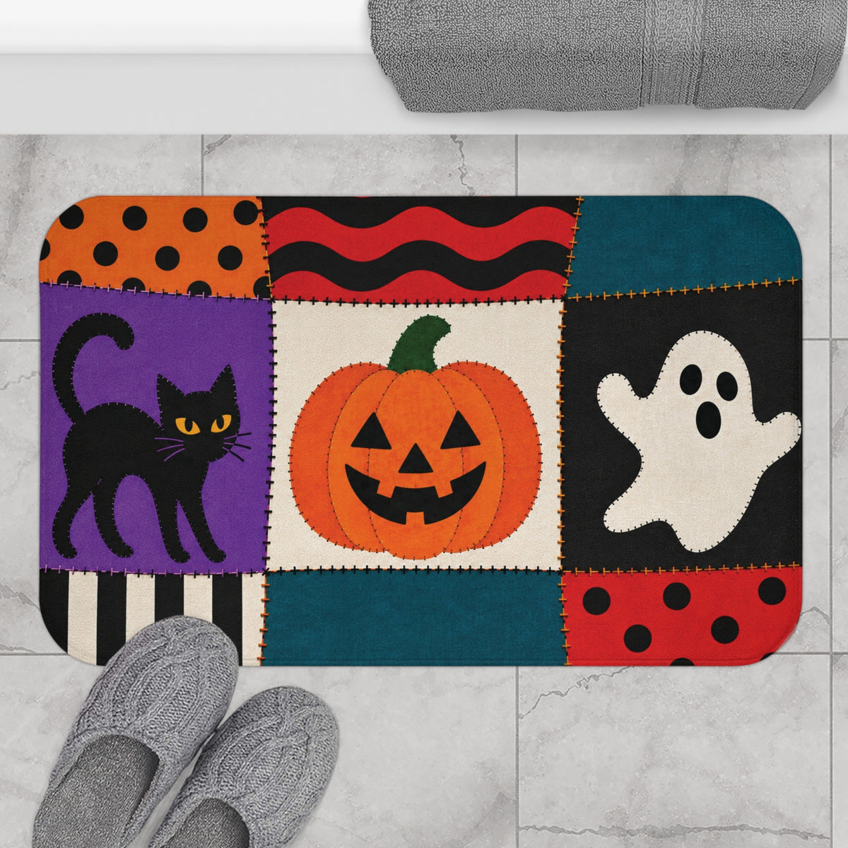 AmazerBath Halloween bath mat featuring patchwork cat, ghost, and jack-o'-lantern placed on light bathroom tile beside a bathtub.