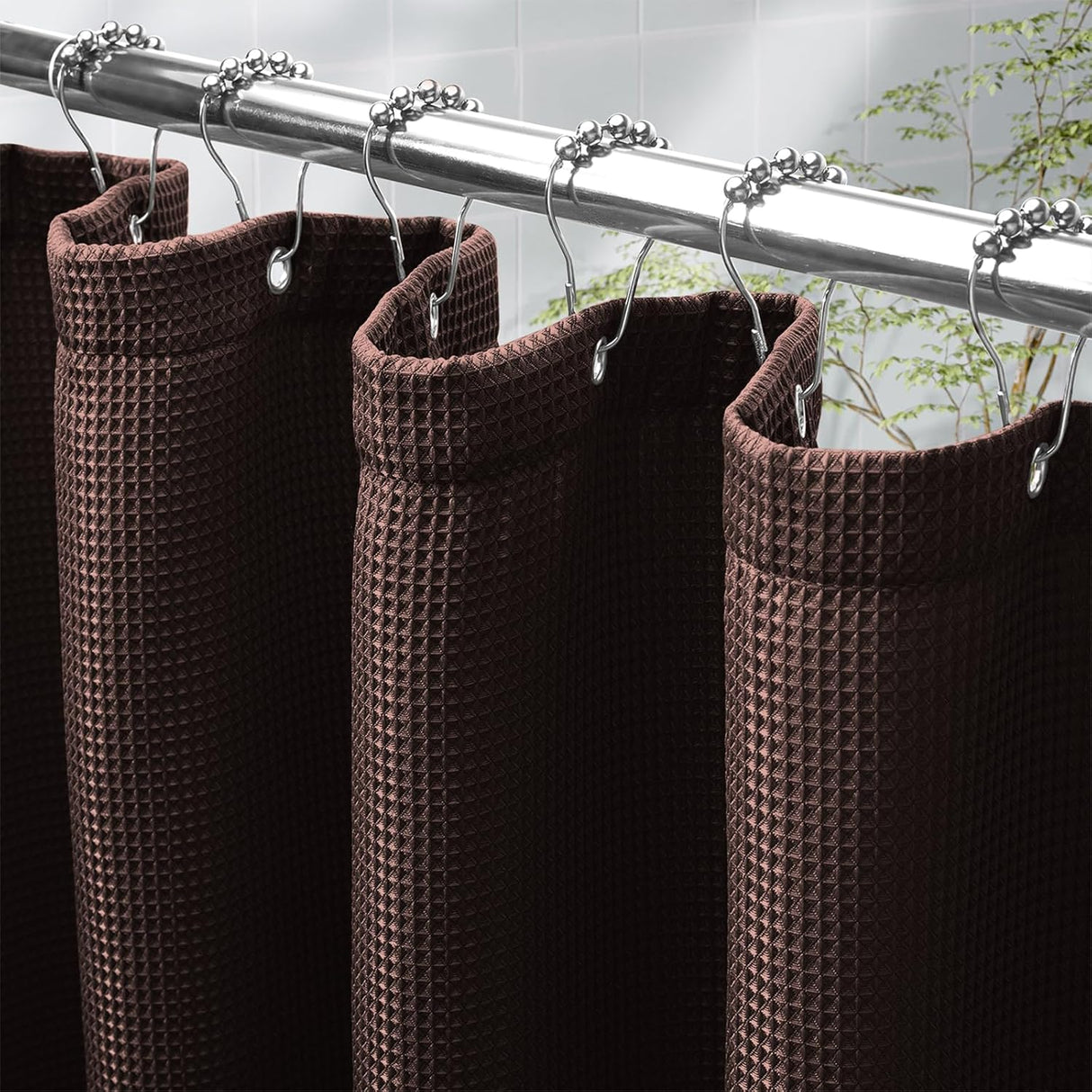 Brown waffle-textured shower curtain with silver hooks on a rod against a tiled wall.