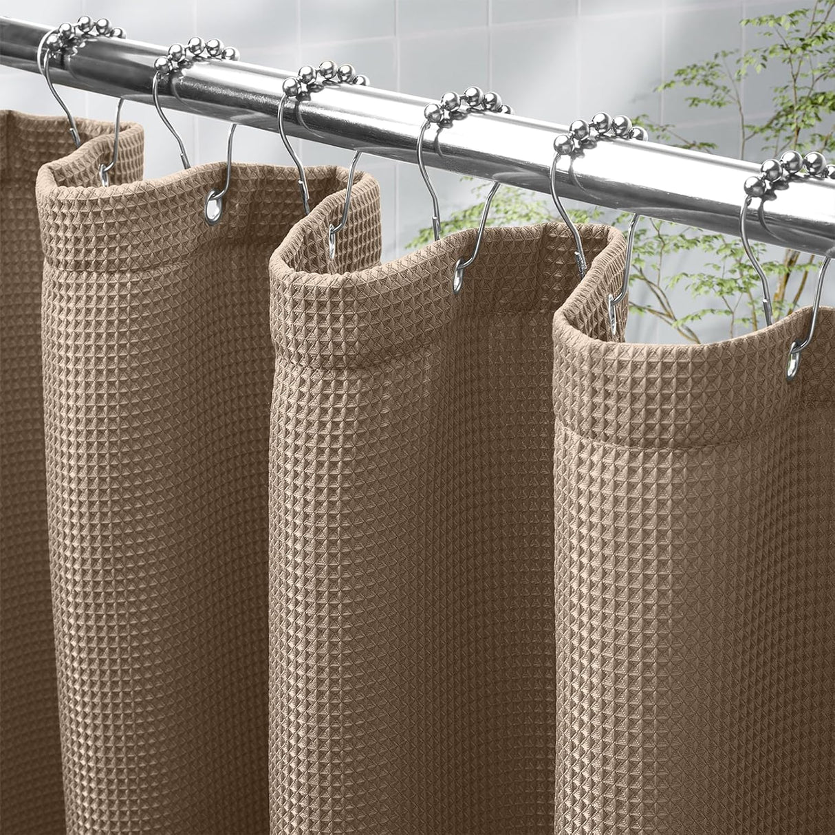 Taupe waffle-textured shower curtain with silver hooks on a rod against a tiled wall.