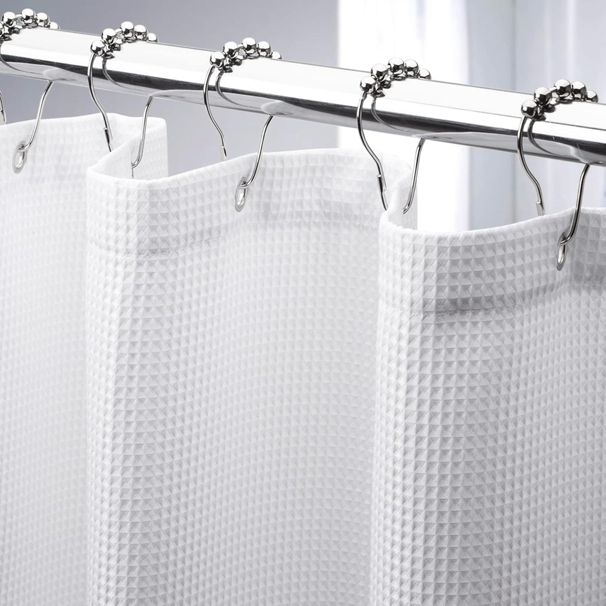 White shower curtain with silver hooks on a gray background