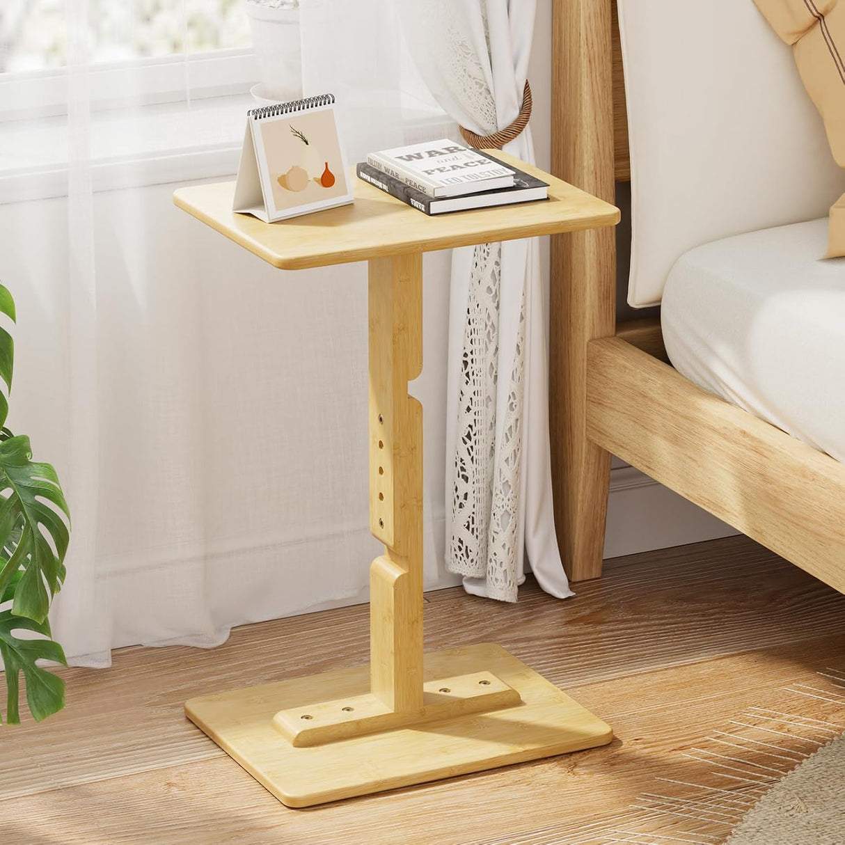 Bamboo side table next to a bed with books and a plant in a bedroom setting.