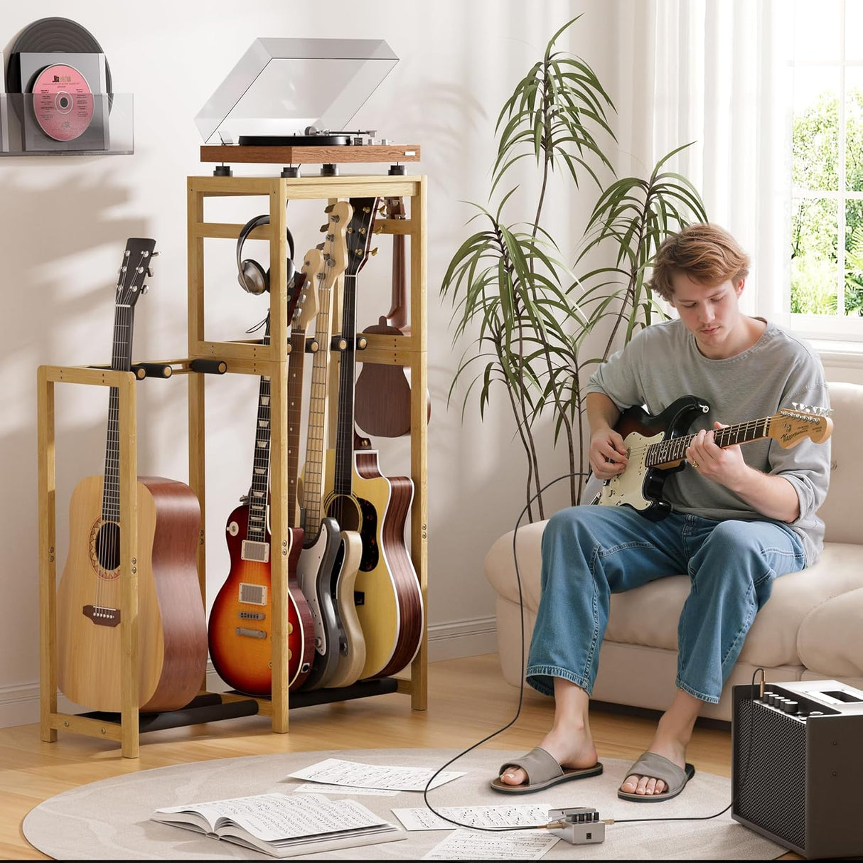 Person playing guitar in a living room with a guitar stand and record player.