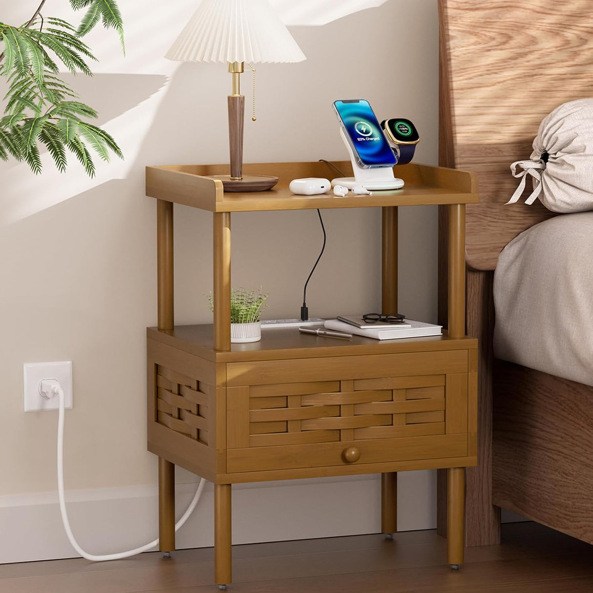 Wooden nightstand with lamp, phone, and other items next to a bed.