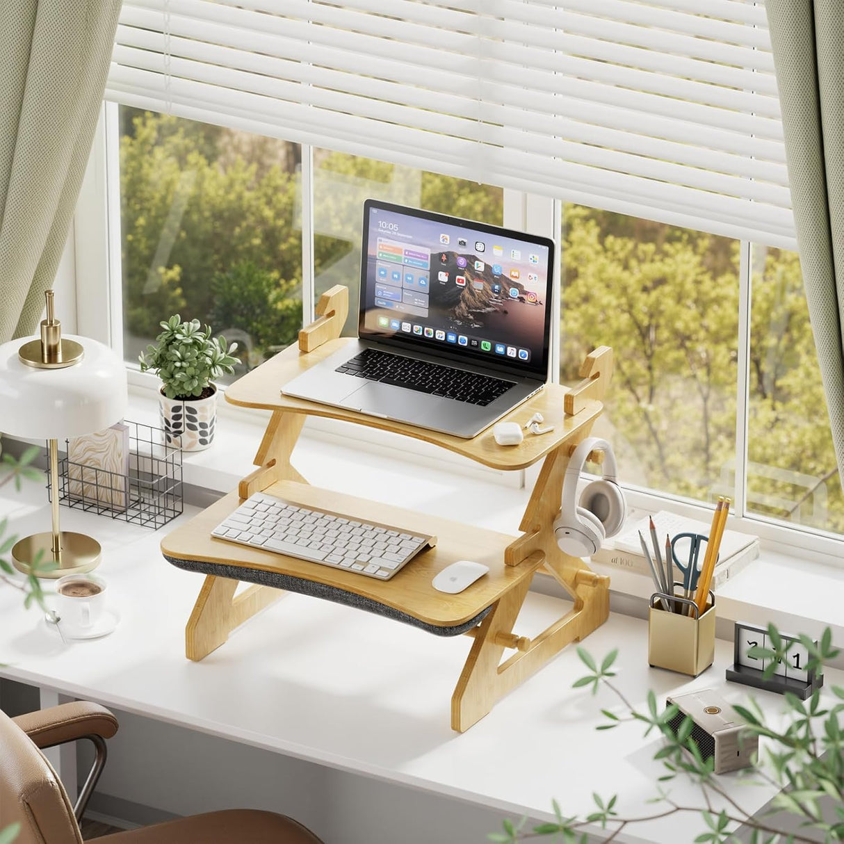 Wooden standing desk converter on a desk with laptop and accessories, near a window.