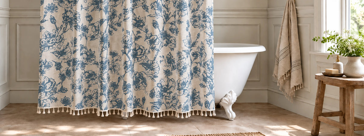 A blue and beige shower curtain hanging in a bright bathroom next to a white clawfoot tub, with a beige towel draped over the side and a small wooden stool holding a potted plant.