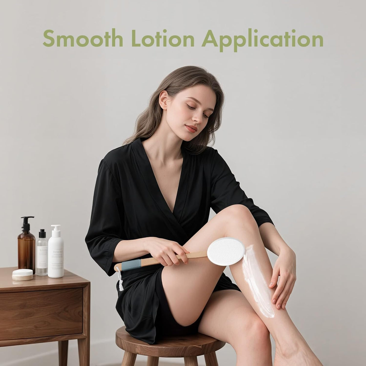 Woman applying lotion to her leg with a brush, sitting on a stool with a neutral background.