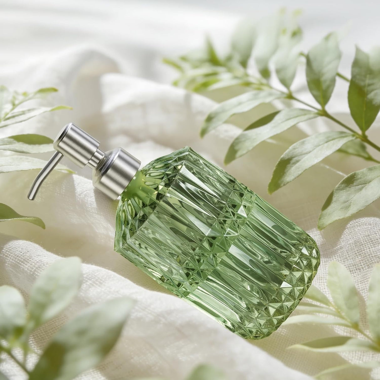 Green diamond-shaped bottle with silver pump on a white fabric background with green leaves