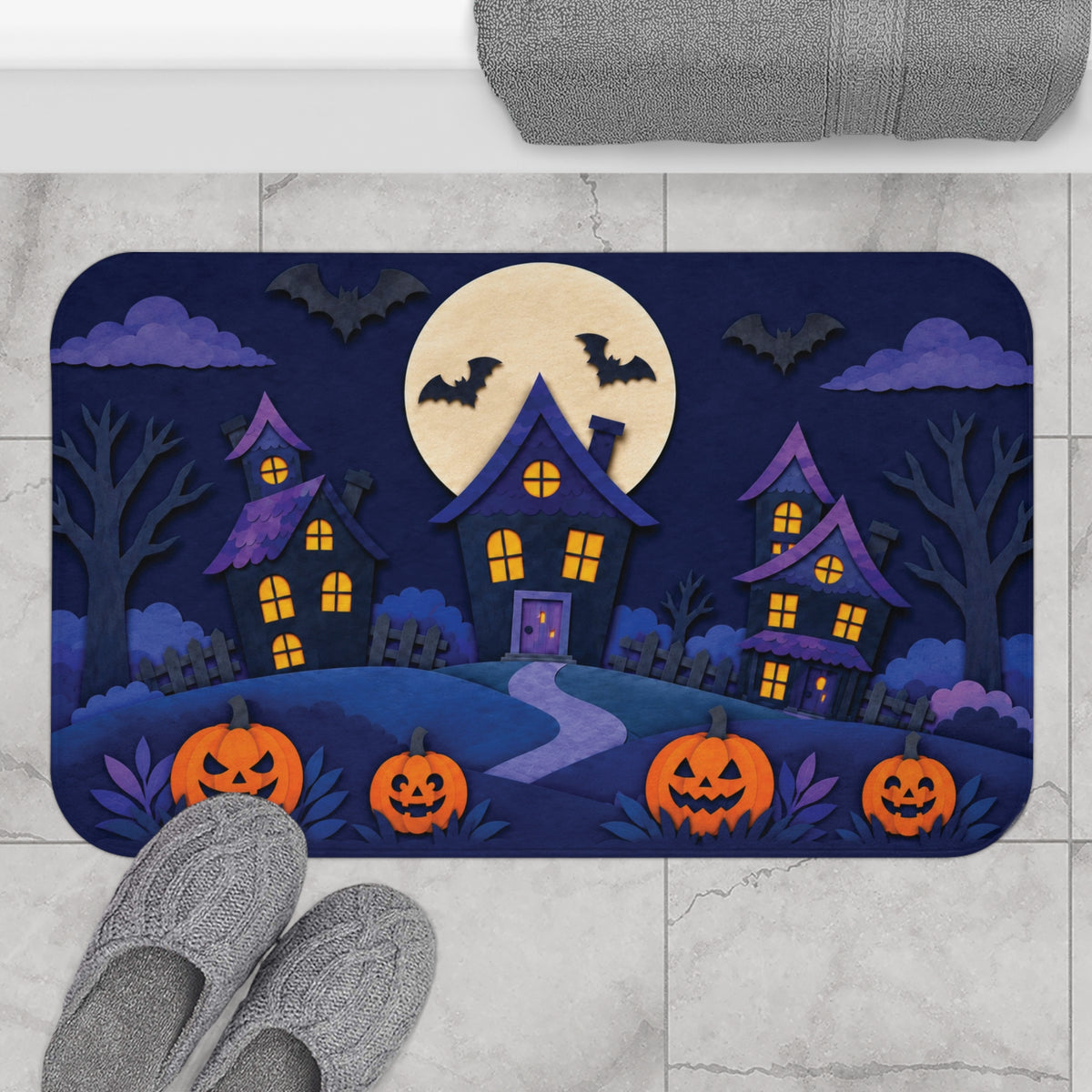 AmazerBath Halloween bath mat featuring haunted houses, full moon, and pumpkins placed on light bathroom tile beside a bathtub.