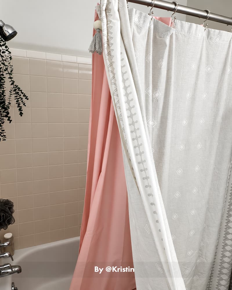 AmazerBath white 120 GSM fabric shower curtain liner layered over a pink curtain beside a tiled bathtub.
