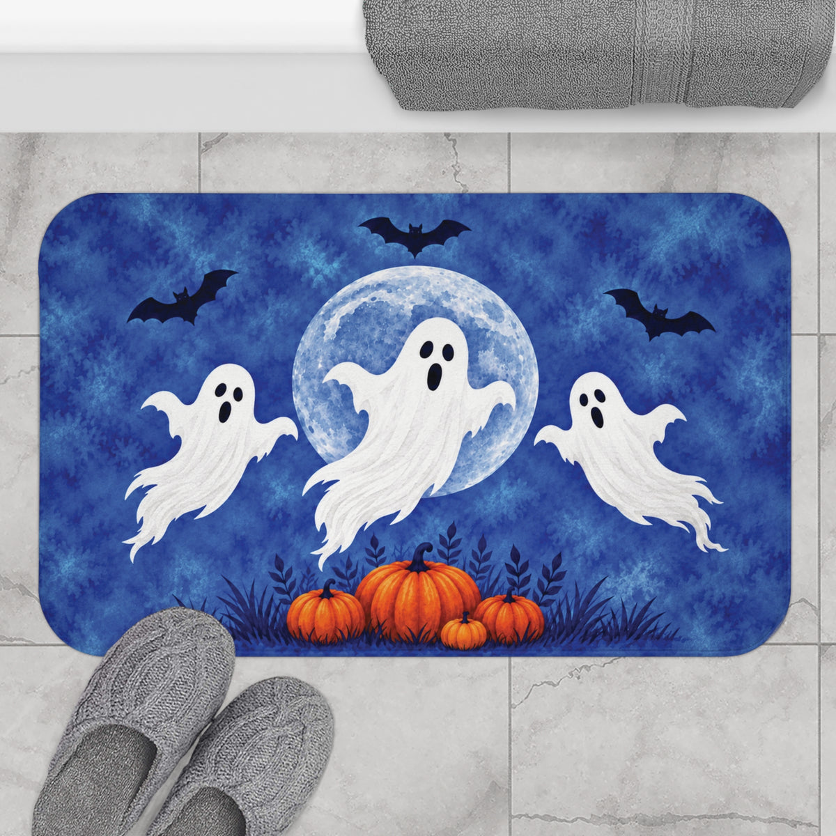 AmazerBath Halloween bath mat featuring blue moon, white ghosts, and pumpkins placed on light bathroom tile beside a bathtub.