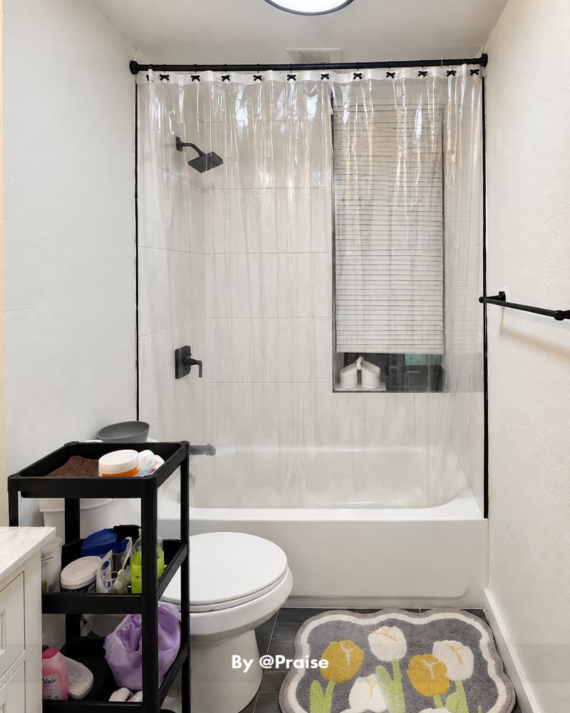 AmazerBath clear 12G PVC shower curtain liner enclosing a bathtub in a compact bathroom with a storage cart.