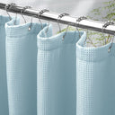 Light blue waffle-textured shower curtain with silver hooks on a metal rod.