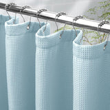 Light blue waffle-textured shower curtain with silver hooks on a metal rod.