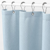 Light blue waffle-textured shower curtain with silver rings on a white background