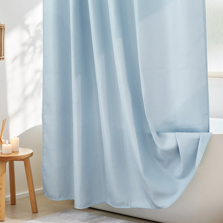 Light blue curtain partially drawn in a room with a wooden side table and candles.