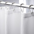 White shower curtain with silver hooks on a gray background