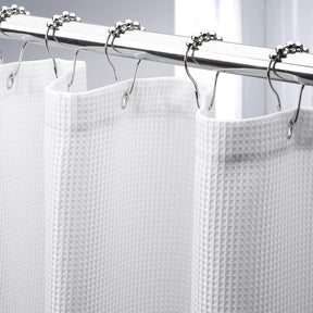 White shower curtain with silver hooks on a gray background