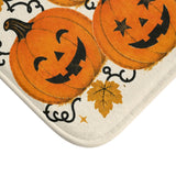 AmazerBath Halloween bath mat corner with orange jack-o'-lantern cluster on cream, vivid print, soft texture, and a bound edge.