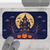 AmazerBath Halloween bath mat featuring haunted house, full moon, and glowing pumpkins placed on light bathroom tile beside a bathtub.
