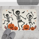 AmazerBath Halloween bath mat featuring dancing skeletons and pumpkins on cream placed on light bathroom tile beside a bathtub.