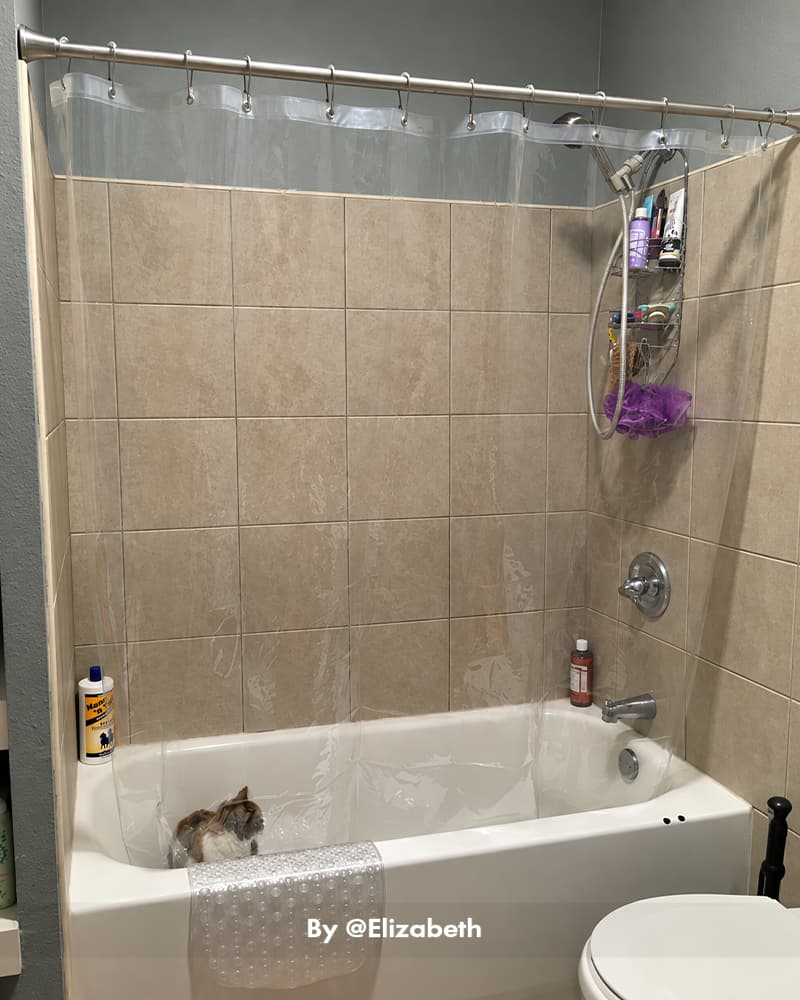 AmazerBath clear 8G PEVA shower curtain liner hanging around a tiled bathtub with a corner shower caddy.