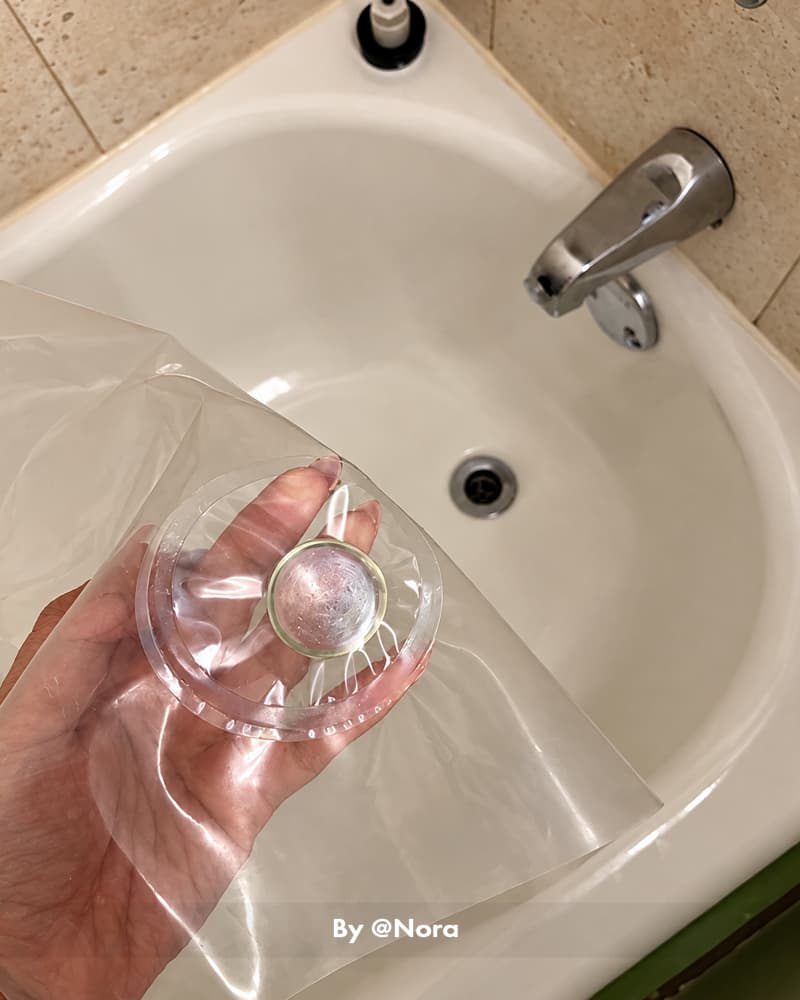 AmazerBath clear 8G PEVA shower curtain liner held over a white bathtub to show its transparent, flexible material.