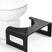 Black step stool in front of a white toilet on a white background