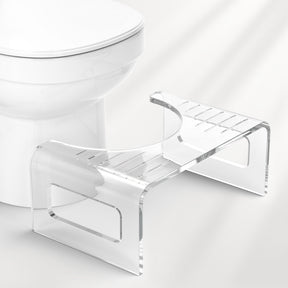 Clear acrylic step stool next to a toilet on a white background