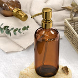 Brown glass bottle with gold pump on a white surface with greenery