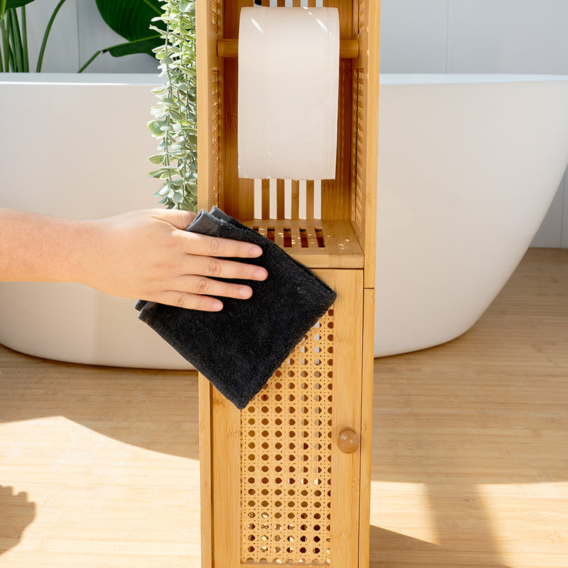 Person holding a black towel in front of a bamboo wooden shelf with a white roll of paper towels, set against a bathroom background.