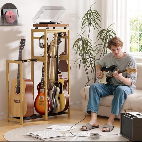 Person playing guitar in a living room with a guitar stand and record player.