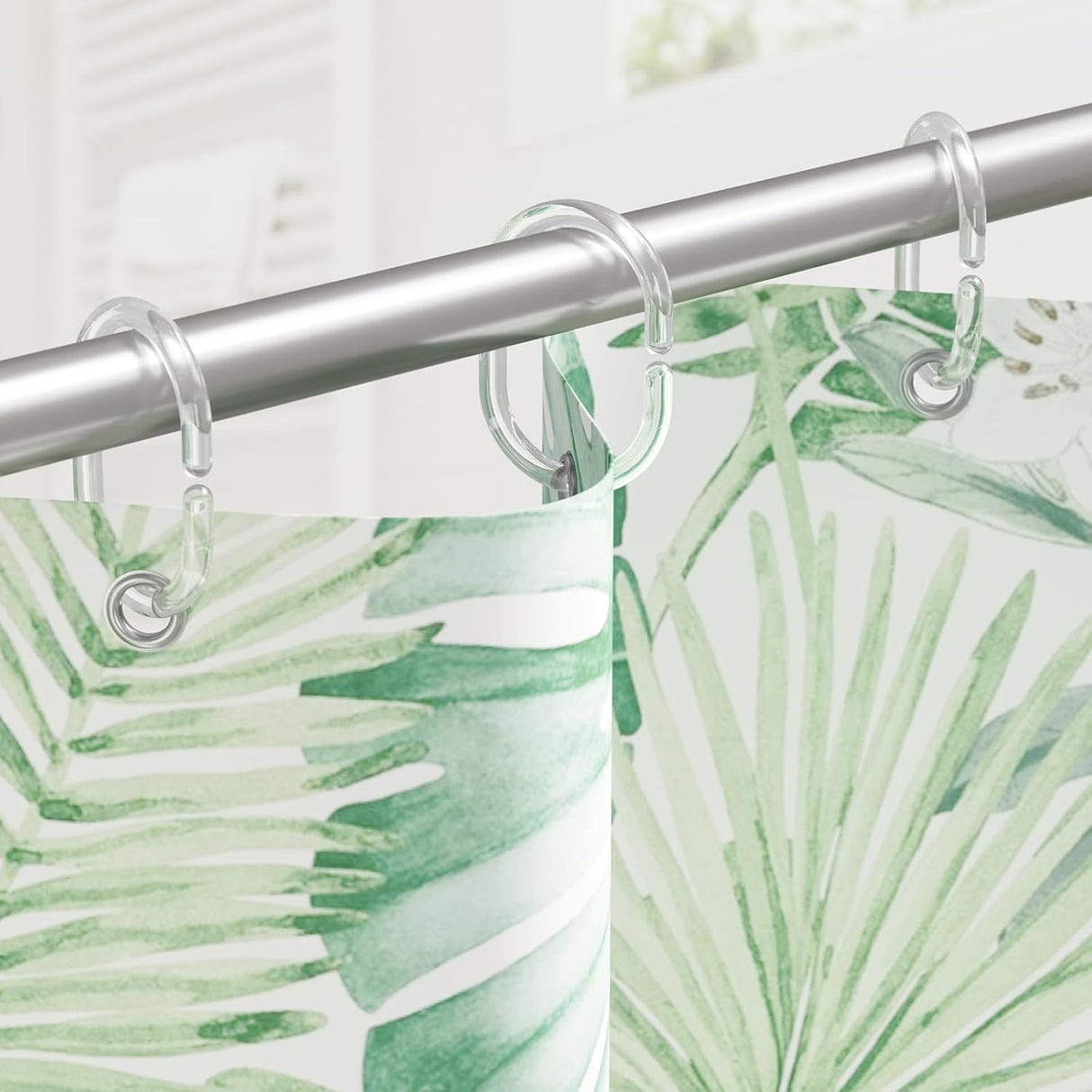 Shower curtain with green leaf pattern and clear hooks on a silver rod.
