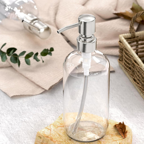 Clear glass soap dispenser with silver pump on a wooden block, light background