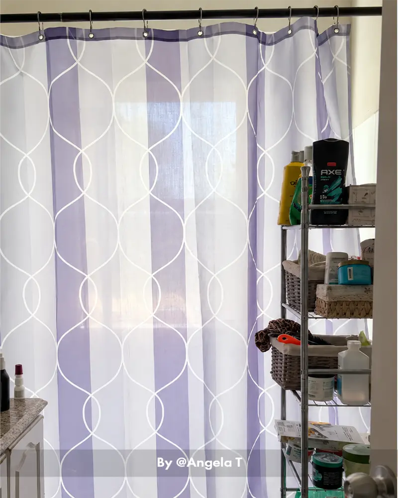 AmazerBath lavender geometric shower curtain with 12 rings filtering window light beside a black storage shelf.