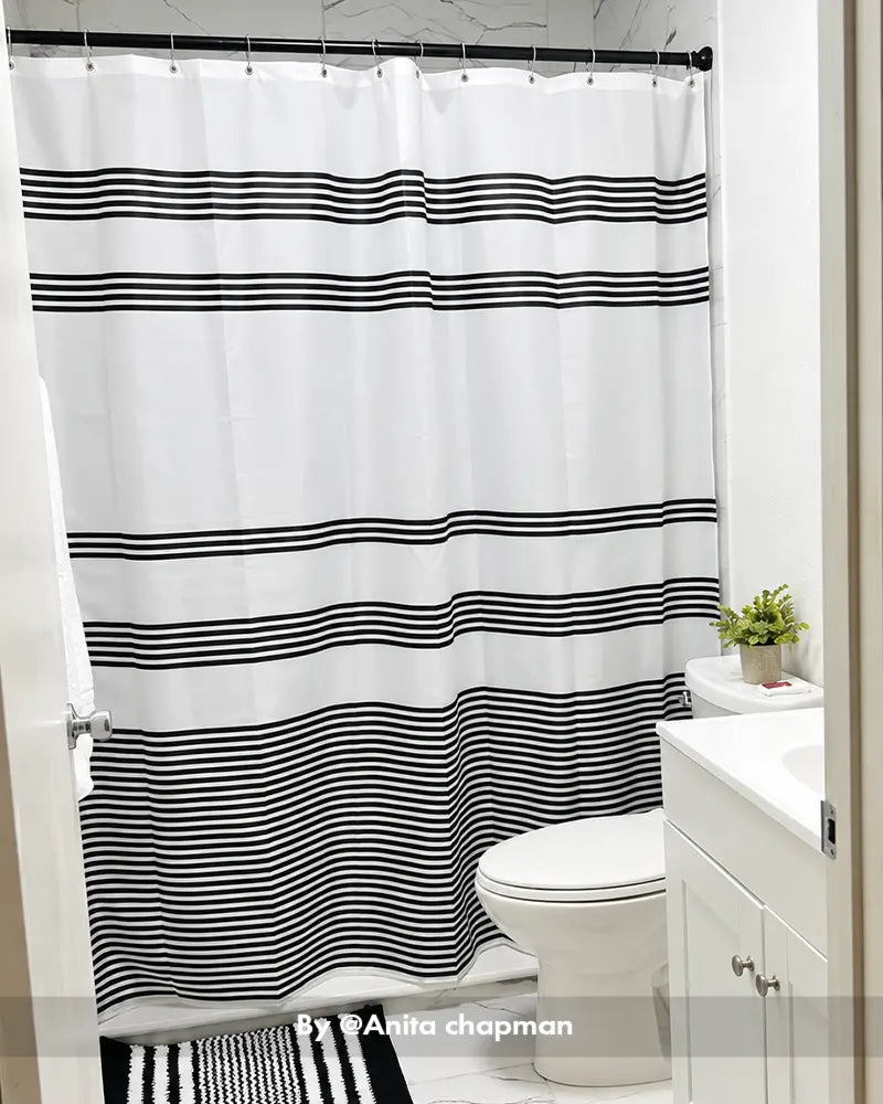 AmazerBath gray striped shower curtain with 12 rings hanging above a white bathtub in a compact modern bathroom.