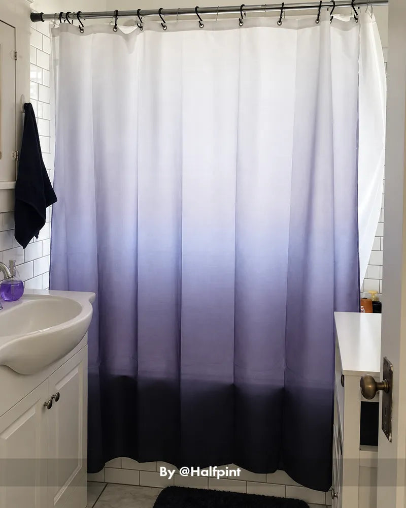 AmazerBath ombre shower curtain fading from white to navy with 12 rings installed across a bright bathtub.