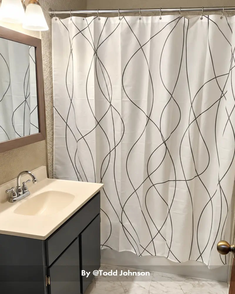 AmazerBath white shower curtain with gray wave pattern and 12 rings installed beside a vanity in a home bathroom.