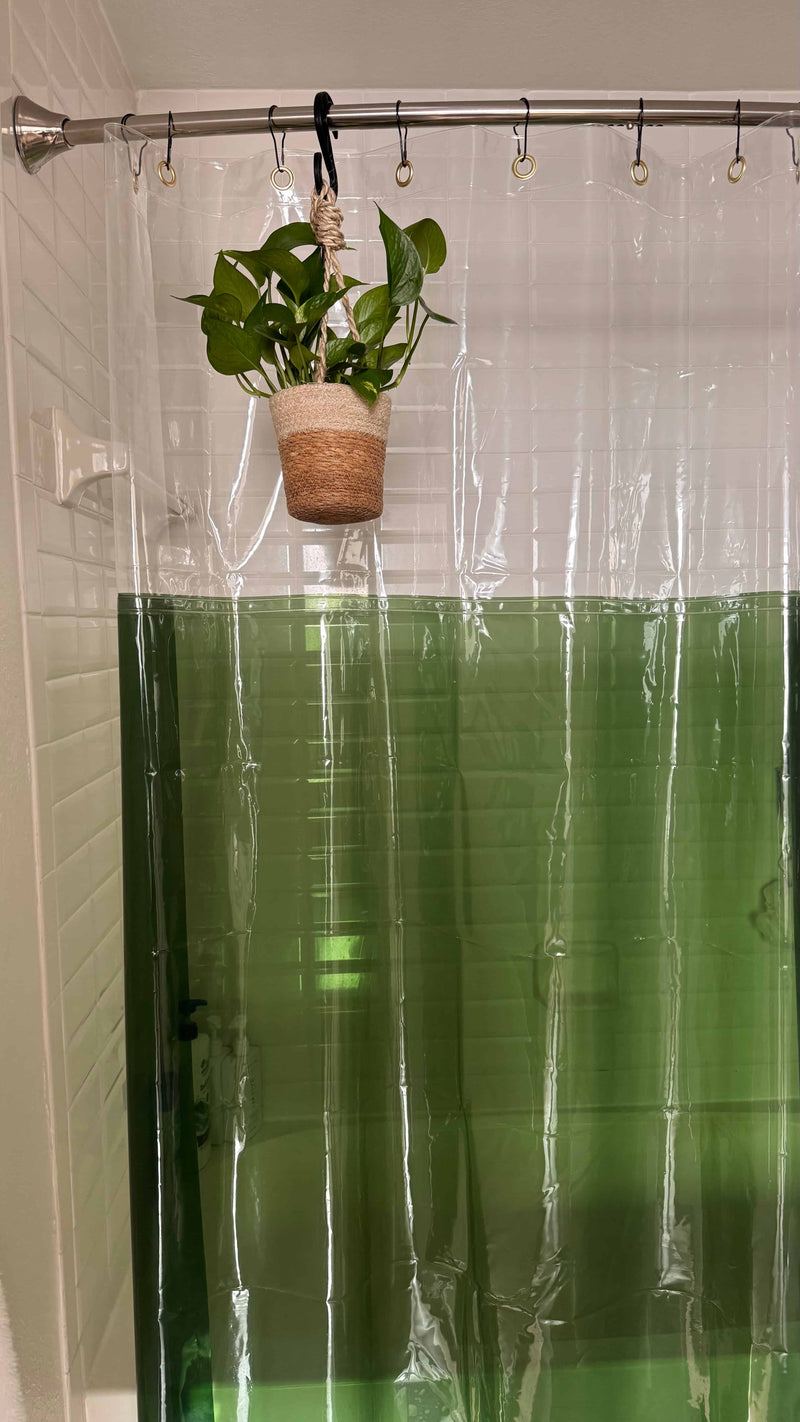 Plant in a pot hanging from a shower curtain rod with a clear shower curtain in the background.