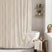 Bathroom with a white bathtub and textured shower curtain, wooden stool with towel, and plants.