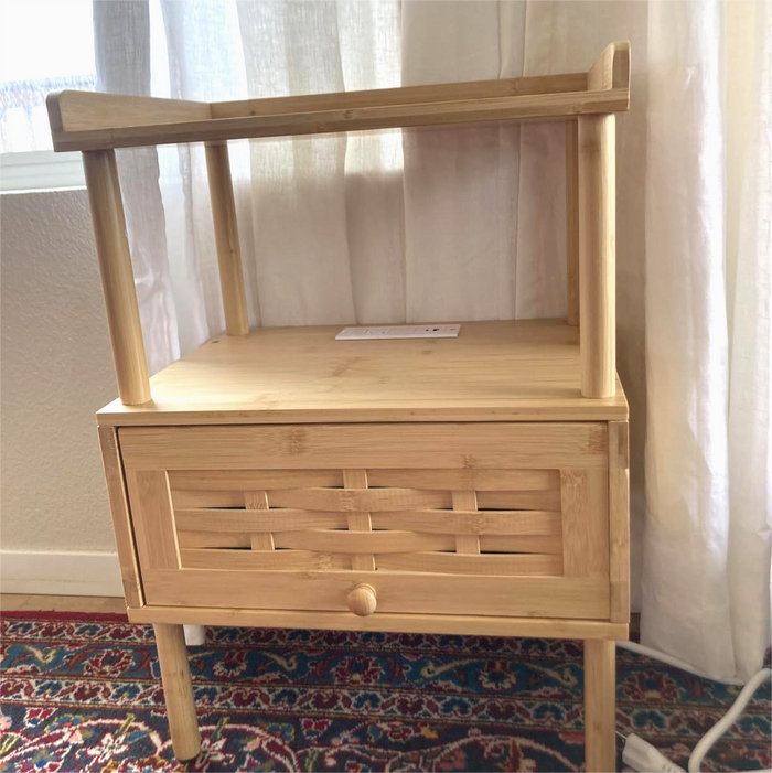 Bamboo wooden nightstand with a drawer in a room with curtains and a rug.