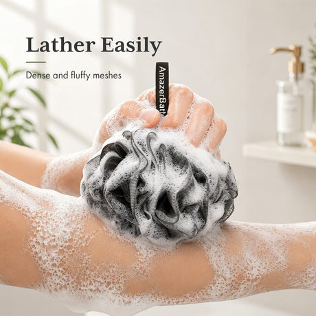 Person using a black bath pouf with foam in a bathroom setting, featuring the brand 'AmazerBath'.