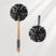 Two black bath pouf scrubbers with wooden handles on a light gray background