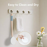 Wall-mounted hooks with a scrubber, towel, and small plant on a neutral background.