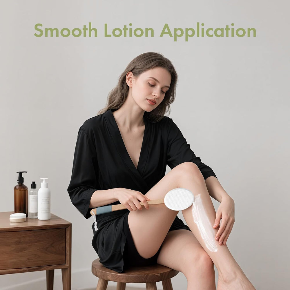 Woman applying lotion to her leg with a brush, sitting on a stool with a neutral background.