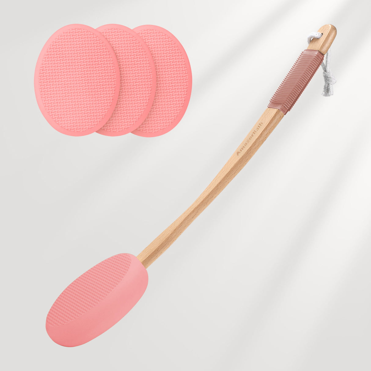 Pink silicone spatula with wooden handle and three additional silicone pads on a light gray background