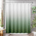 Green and white gradient shower curtain in a bathroom setting with plants and a table.