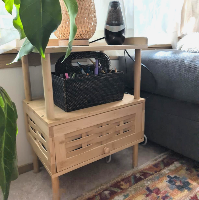 Wooden side table with a black woven basket containing stationery items, next to a sofa and plant.
