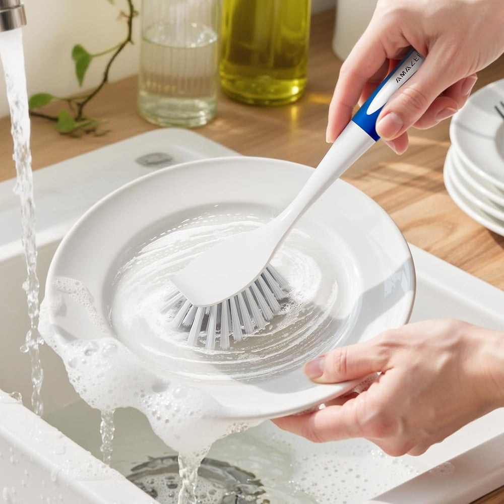 Person washing a white plate with a brush under running water in a kitchen sink.