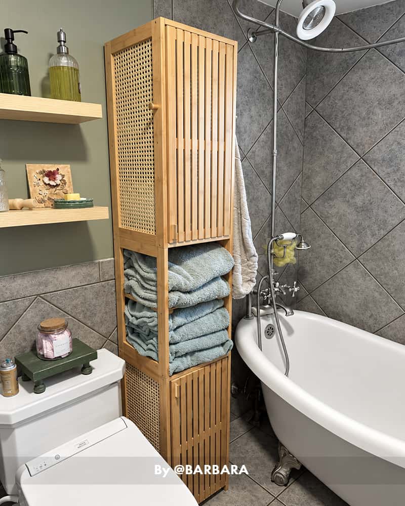 AmazerBath slim bamboo bathroom storage cabinet storing folded blue towels beside a freestanding bathtub.