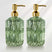 Two green glass soap dispensers with gold pumps on a white background